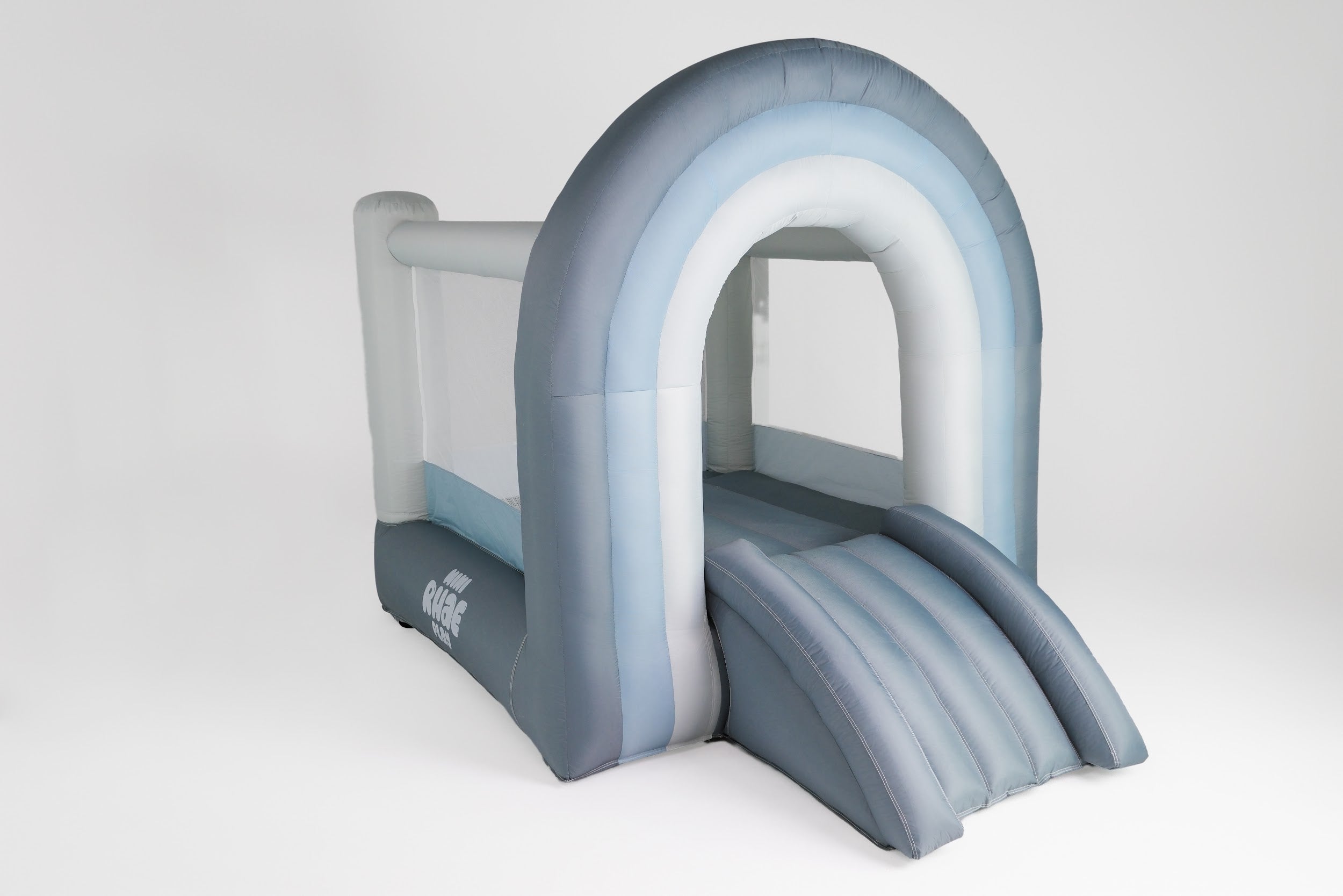An inflatable bounce house with a rainbow arch, designed for children's play. The bounce house is white, with entry steps and a spacious interior.